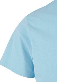 T-shirt en coton bleu clair montrant l'épaule et la manche avec une texture lisse et des coutures renforcées. Design classique à manches courtes.