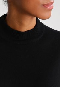 Maglione nero a coste con un design a collo alto, che mostra una consistenza morbida e una silhouette aderente, adatto per essere indossato a strati.