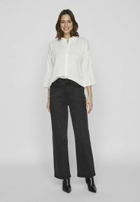Vit oversized knäppt skjorta med strukturerad finish, kombinerad med högmidjade svarta jeans och spetsiga svarta ankelskor.