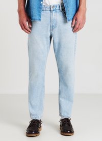 Jeans in denim blu chiaro con vestibilità rilassata, caratterizzati da una texture sbiadita, design classico a cinque tasche e chiusura con zip. Indossati con scarpe scure.