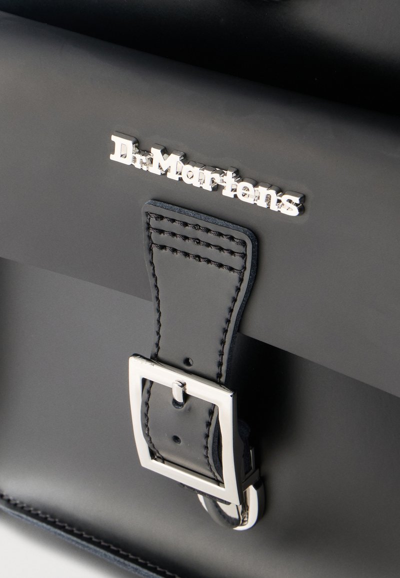 Black Dr. Martens bag with silver buckle and stitched leather strap, featuring embossed brand logo on smooth surface.