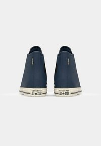 Blauwe hoge sneakers met een canvas bovenwerk, rubberen zolen en contrasterende witte strepen. Heeft een zwart logo aan de zijkant en textuuraccenten.