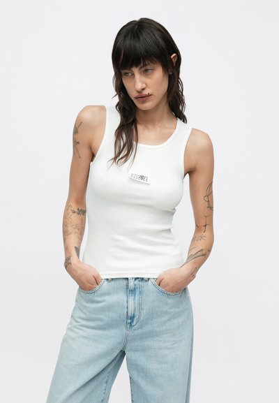 Λευκό ριμπ αμάνικο τοπ με στρογγυλή λαιμόκοψη και κεντρική ετικέτα, σε συνδυασμό με τζιν παντελόνι ανοιχτού μπλε χρώματος. Ομαλή υφή και εφαρμογή που αγκαλιάζει το σώμα.