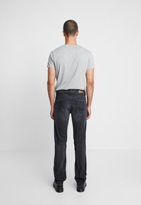 Černé džíny z denimu se střihovým provedením do rovna, s koženou etiketou na pasu, prezentované s šedým tričkem. Hladká textura, minimální design.