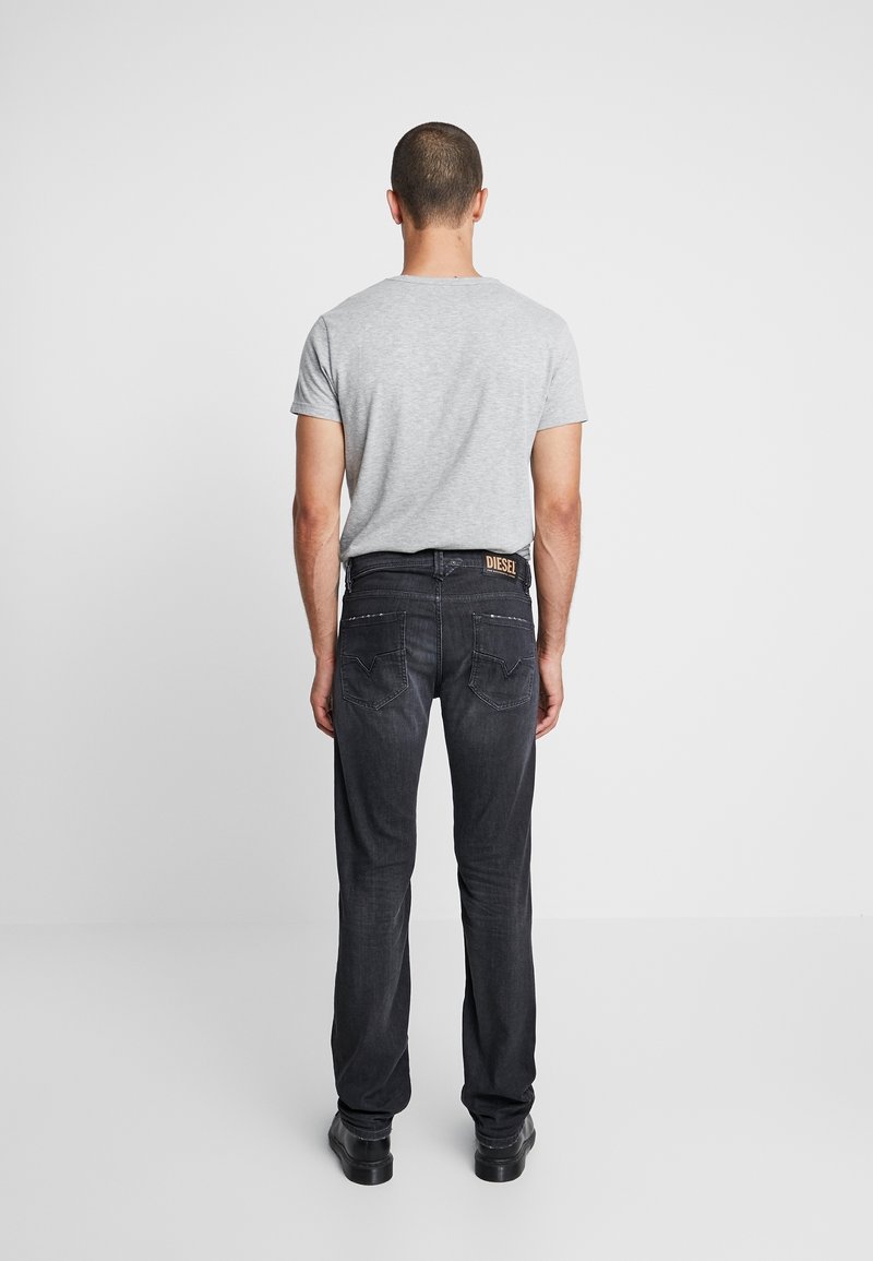 Černé džíny z denimu se střihovým provedením do rovna, s koženou etiketou na pasu, prezentované s šedým tričkem. Hladká textura, minimální design.