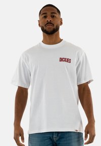 Balta medvilninė marškinėliai trumpomis rankovėmis su raudonu "DICKIES" logotipu kairėje krūtinės pusėje. Paprastas, klasikinis dizainas su apvalia iškirpte.