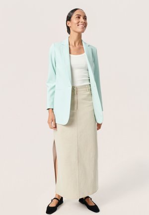 Hellblaues Blazer, weißes Tanktop, beiger Jeans-Maxi-Rock mit Schlitz und schwarze Ballerinas. Glatte Textur und maßgeschneiderter Schnitt.