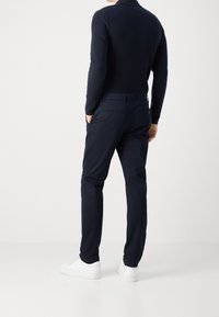 Pantaloni blu navy con una vestibilità slim, texture liscia e due tasche posteriori; indossati con sneaker bianche e un maglione nero aderente.