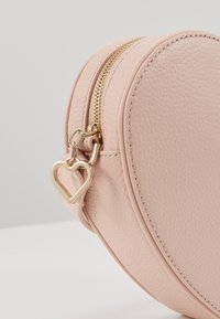 Owalna torba z różowego ekoskóry o teksturowanej powierzchni, ze złotym zamkiem błyskawicznym i uchwytem w kształcie serca.