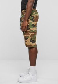 Kamuflage cargo shorts i grøn, brun og sort, med elastisk talje, sidelommer og knælangt snit. Kombineret med hvide sneakers.
