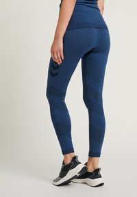 Granatowe legginsy o dopasowanym kroju, z teksturowanymi wzorami i paskowymi akcentami w kontrastowym odcieniu. Noszone z butami sportowymi.