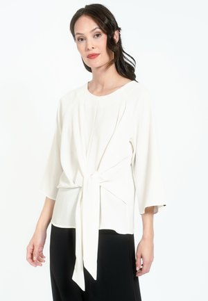 White blouse with a round neckline, three-quarter sleeves, and a tied knot detail at the waist, made from a smooth, lightweight fabric.