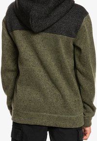 Sudadera de color verde oliva con un tejido texturizado y paneles de hombro negros con patrón. Cuenta con una capucha con cordón y bolsillos tipo canguro.