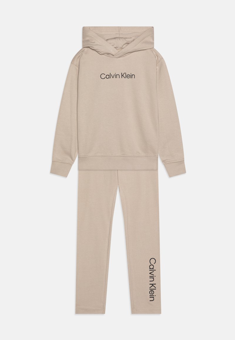 Bežová mikina s kapucňou a zodpovedajúce legíny. Mäkká tkanina s tmavým potlačou loga "Calvin Klein" na oboch kusoch. Pohodlný, štíhly strih.