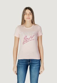Camiseta de algod�ón rosa claro con mangas cortas, que presenta un logo triangular de "GUESS" y el texto brillante "Love" en color rosa. Diseño ajustado, textura suave.