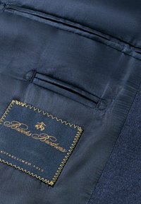 Námořnická tkanina s hladkým povrchem má na sobě štítek přišitý zlatou nití, na němž je napsáno "Brooks Brothers" a "Established 1818."