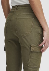 Pantalons cargo vert olive avec une taille ajustée, un tissu texturé et de multiples poches, y compris une poche rabat sur la cuisse.