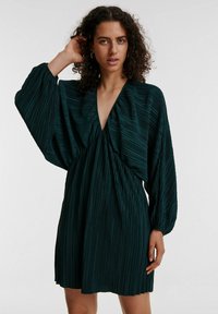 Dunkelgrünes, gefältetes Minikleid mit V-Ausschnitt, gepufften langen Ärmeln und taillierter Taille. Aus glattem Stoff gefertigt, verfügt es über einen schwingenden Rock.
