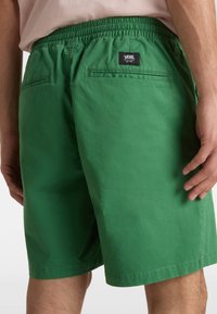 Grønne bomuldsshorts med elastisk talje, to baglommer og et sort Vans-logo mærke bagpå. Glat tekstur, afslappet design.