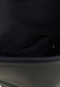 Mustan värinen laukku, jossa on tekstuurilla varustettu vetoketjupussi. Ympäröivä materiaali on sileää, mikä parantaa järjestystä ja saavutettavuutta.