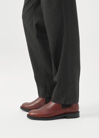 Bottes Chelsea en cuir marron avec une finition lisse et des panneaux latéraux élastiques, associées à un pantalon à rayures fines gris foncé. Semelles en caoutchouc noir plat.