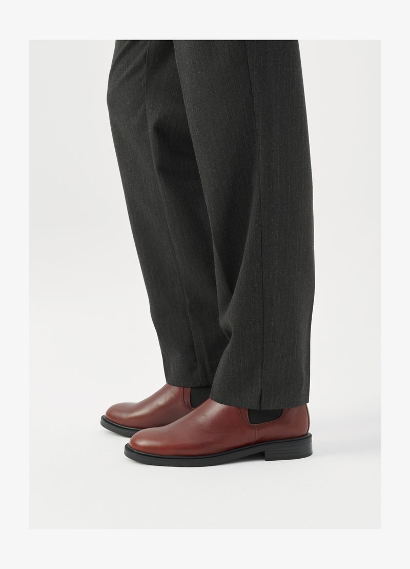 Bottes Chelsea en cuir marron avec une finition lisse et des panneaux latéraux élastiques, associées à un pantalon à rayures fines gris foncé. Semelles en caoutchouc noir plat.