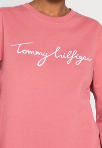 Felpa rosa in cotone, con un logo ricamato bianco che riporta "Tommy Hilfiger" sul petto. Collo a giro e maniche lunghe.