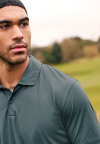 Polo shirt vert foncé en tissu texturé avec un motif subtil, doté d'un col lisse et d'une patte de boutonnage à deux boutons.