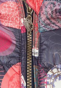 Gevoerde jas met een meerkleurig patroon in roze, paars en blauw tinten. Messing ritssluiting met een unieke egelvormige trekker.