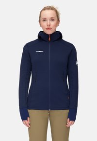 Navy blue insulated jacket with a high collar and hood, featuring zippered side pockets and orange accents on the zipper. Textured fabric.