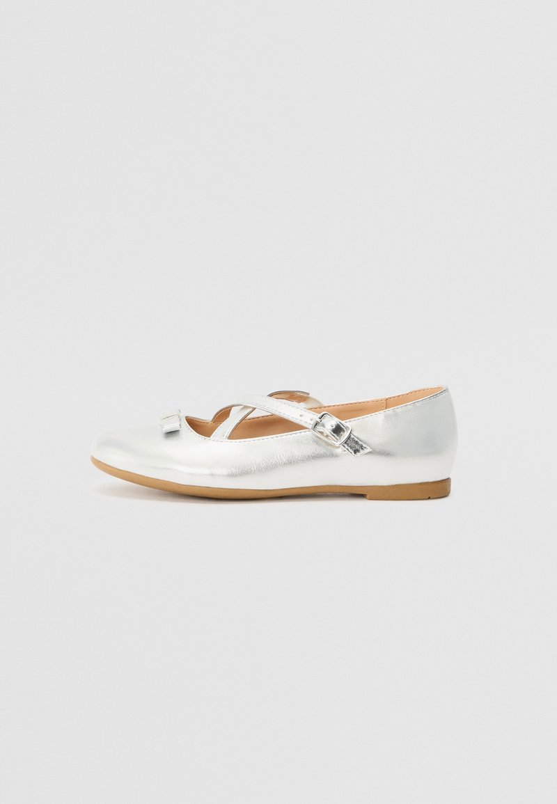 Chaussure plate Mary Jane argentée brillante avec une bride à boucle et un petit nœud décoratif sur une semelle marron clair, sur un fond gris uni.