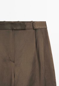 Bruine broeken met een gladde textuur, voorzien van een brede tailleband, plooien en zijzakken. De stof lijkt lichtgewicht en zacht te zijn.