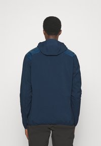 Mörkblå huvjacka, tillverkad av mjukt material med en slät yta. Har kontrasterande blå detaljer på axlarna och en avslappnad passform.