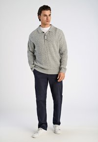 Harmaa neulepusero, jossa on kauluksellinen kaula-aukko ja kaksi nappia. Yhdistetty tummansinisiin housuihin ja valkoisiin tennareihin. Yksinkertainen, rento asu.