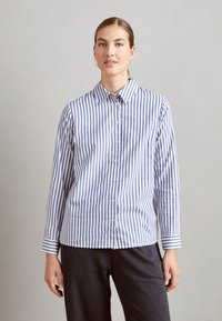 Camicia a righe blu e bianca in cotone. Presenta un colletto a punta e maniche lunghe con polsini abbottonati. Retro semplice e senza tasche.