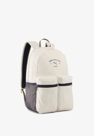 Sac à dos Puma crème avec deux poches avant zippées, poche latérale en mesh, bretelles rembourrées et logo Puma Athletics sur le compartiment principal.
