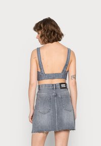 Top cropped de denim com alças largas, apresentando um padrão riscado. Combinado com uma saia mini de denim cinza com barra desfiada e bolsos traseiros.
