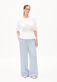 Witte peplumtop met geplooide taille, gecombineerd met lichtblauwe wijde broek en zilveren schoenen. Soepele stof en een ontspannen pasvorm.