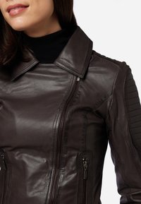 Braune Lederjacke mit Kragen, Reißverschluss vorne und seitlichen Taschen; verfügt über gesteppten Akzente an den Schultern und eine glatte Textur.