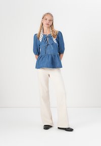 Denim peplum top s puff rukávmi, s kravátkou na krku a bodkovaným šálom. Vhodné k krémovým rozšíreným nohaviciam a čiernej obuvi.