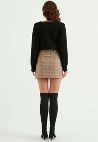 Maglione nero corto, minigonna beige in tessuto intrecciato e stivali neri alti sopra il ginocchio con tacco. Texture lisce, design minimalisti e colori neutri.