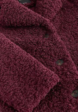 Burgunderfarbenen Fleece-Mantel mit strukturiertem Material, ausgestattet mit einem Schalkragen und dunklen Knöpfen, faltig dargestellt, um Details und Tiefe zu zeigen.
