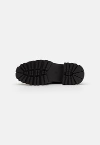 Black rubber shoe sole with distinct deep tread pattern. Features a flat surface with rounded edges. Lightweight and sturdy construction.