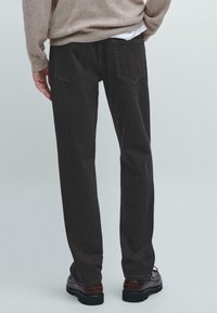Dark gray denim jeans with a straight-leg design, visible stitching, and two back pockets, worn with brown shoes and a beige sweater.