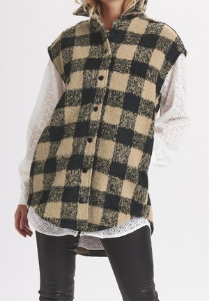 Geruit vest in beige en zwart, gemaakt van textuurstof, met een hoge kraag, knopen aan de voorkant en oversized armopeningen, gedragen over een wit kanten shirt.