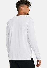 T-shirt bianco a maniche lunghe con scollatura rotonda, fenditure laterali sottili e dettagli riflettenti sulla parte superiore della schiena. Tessuto dalla consistenza liscia.