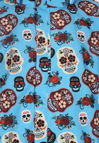 Blauer Stoff mit einem sich wiederholenden Muster aus bunten Zuckerschädeln und Rosen, ergänzt durch florale Akzente und schwarze Blättermuster.