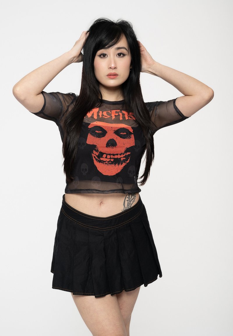 Black sheer cropped top featuring a red skull graphic with the text "Misfits." Paired with a black pleated skirt, emphasizing texture and contrast.