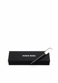 Čierne kovové pero s texturovaným úchopom, striebornými detailami a bielym akcentom. Obsahuje čiernu škatuľku s bielym textom "HUGO BOSS".