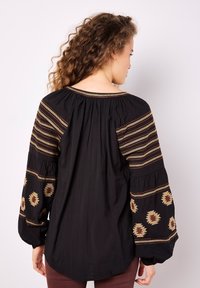 Blusa nera con maniche lunghe a sbuffo, con motivi ricamati oro e ruggine sulle spalle e sulle maniche, realizzata in tessuto leggero.